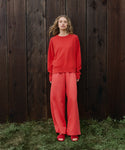 Woman wearing a red outfit standing against a wooden fence.