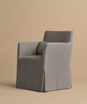 The Sunset Dining Arm Chair features a modern design with a grey slipcover, square arms, and a slightly reclined backrest, shown against a plain beige background.