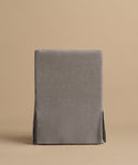 The Sunset Dining Arm Chair features a straight back and a fitted gray slipcover with subtle seams and two side slits, shown from the back against a plain beige background.