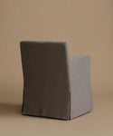 A single upholstered armchair shown from the back, covered in a dark gray fabric with a matching gray skirted base, photographed against a plain warm beige studio background.