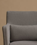 Close-up of a gray upholstered armchair with a matching rectangular pillow against a warm beige background.