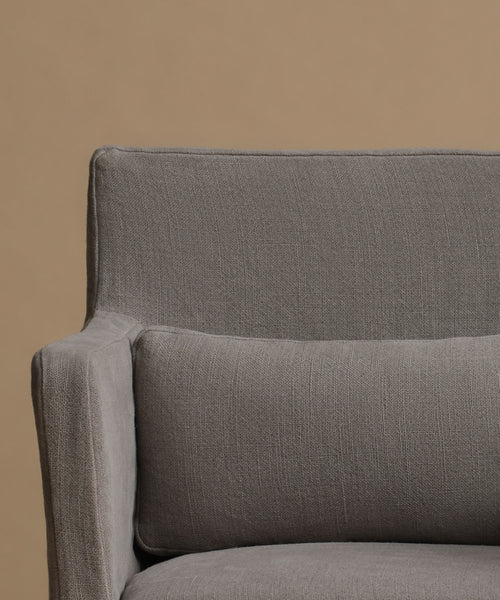 Close-up of a gray upholstered armchair with a matching rectangular pillow against a warm beige background.