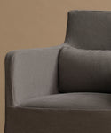 Close-up of a modern armchair upholstered in textured gray fabric, showing the armrest, backrest, and seat cushion against a warm beige background.