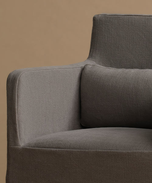Close-up of a modern armchair upholstered in textured gray fabric, showing the armrest, backrest, and seat cushion against a warm beige background.