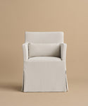 The Sunset Dining Arm Chair, shown front-facing against a plain beige background, features a high back, light beige linen upholstery, straight armrests, a matching lumbar pillow, and a skirted bottom for an elegant look.