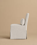 The Sunset Dining Chair features a modern armless design with light beige linen upholstery, a square seat, tall back, and round lumbar cushion, set against a tan background that showcases classic California style.