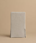 The Sunset Dining Chair, featuring a light beige linen removable slipcover with two front corner slits, is shown against a plain beige background.