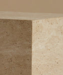A close-up of a travertine stone coffee table showing its natural beige and cream porous texture under warm, soft lighting.