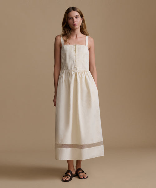 Woman wearing an ivory dress and sandals against a beige backdrop.