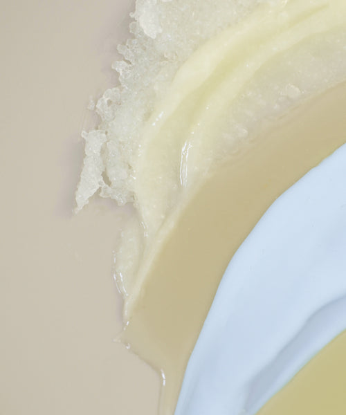 A close-up of The Body Routine shows creamy beige, white, and light blue layers—smooth and grainy in texture—blended on a neutral background, evoking luxurious beauty and essential skincare rituals.