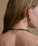 Close-up of a person wearing a green beaded necklace and earrings against a beige background