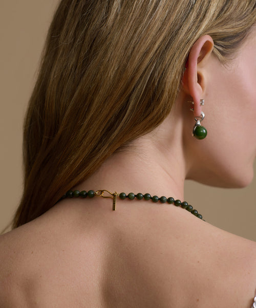 Close-up of a person wearing a green beaded necklace and earrings against a beige background