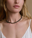 Woman wearing a dark green beaded necklace against a neutral background