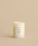 A Topanga Glass Candle rests in a minimalist white container on a beige background. The label reads jenni kayne, Green Leaves, Blackwood, Grapefruit. This natural candle is hand-poured in Los Angeles, 10oz / 295g.
