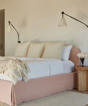 The Cove Bed, featuring a linen-upholstered headboard, is complemented by plush pillows and a bedside lamp to create a serene atmosphere.