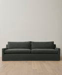 The Harbor Sofa is a modern piece in dark gray linen, featuring two seat and two back cushions. It’s shown against a light wall and set on a light wood floor.