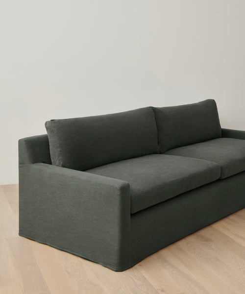 The Harbor Sofa, crafted in Los Angeles with dark gray linen and two seat cushions, features clean lines and sits against a light wall on pale wood flooring.