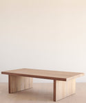 A minimalist wooden coffee table with a rectangular top and sturdy legs, set against a simple backdrop, is easily protected when needed by the Outdoor Vista Coffee Table Cover.