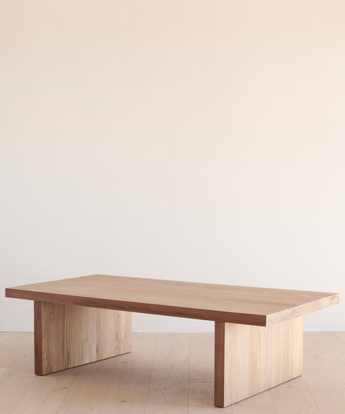A minimalist wooden coffee table with a rectangular top and sturdy legs, set against a simple backdrop, is easily protected when needed by the Outdoor Vista Coffee Table Cover.