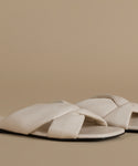 Pair of beige sandals with criss-cross straps on a beige background