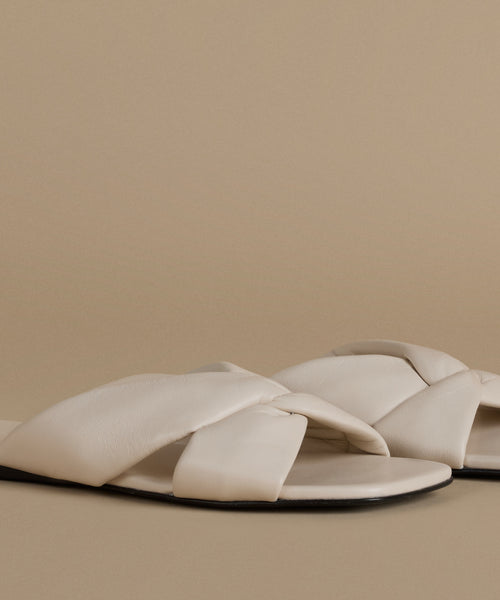 Pair of beige sandals with criss-cross straps on a beige background