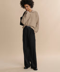 A woman with curly hair wears Wool Jones Trouser and a beige sweater, black shoes, and carries a black shoulder bag while standing against a plain beige background.