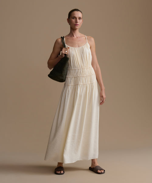 Woman wearing a cream wynn dress holding a black handbag against a beige background