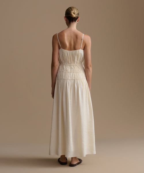 Woman wearing a long, cream wynn dress against a beige background