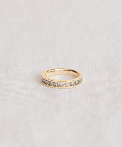 The Stevie Grey Diamond Band showcases a row of round-cut diamonds set along its gold band, beautifully displayed on a light, textured surface.