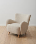 A chair in Bone Sherpa fabric with textured, cream upholstery and curved armrests stands on light wooden legs atop a pale floor, reflecting the cozy appeal of our Aspen Sofa collection. Featured fabric: Fabric Swatch Bone Sherpa.