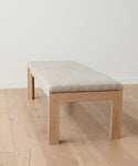 The Otto Bench, crafted in white oak with a light beige wool boucle seat, rests on a light wood floor against a plain white wall.