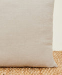 A close-up of the Linen Pillow in light beige natural linen with a smooth texture and feather down insert, displayed on a woven, natural-colored mat against an off-white background for a soft, neutral look.
