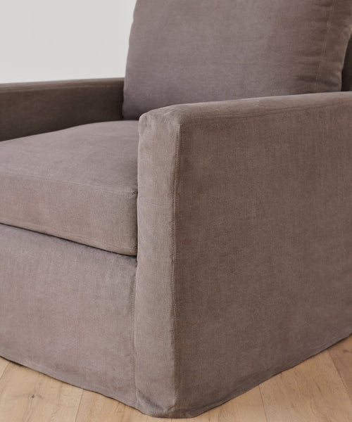 A close-up of a modern upholstered armchair in Fabric Swatch Charcoal Linen with plush seat, straight armrests, and set on a light wood floor—an elegant piece inspired by Jenni Kayne Furniture.