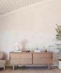 The Mandeville Credenza showcases a lamp, books, bowl, vases, and a small plant against a light wall in a modern space with a neutral palette.