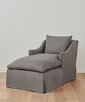 The Miramar Chaise Slipcover, in sleek gray Belgian linen, covers a modern chaise with cushioned seat, backrest, and arms, set on a light wooden floor against a plain white wall.
