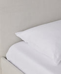 A close-up of the Pacific Bed, featuring a neatly made bed with a white pillow and sheet, set against a light beige upholstered headboard and complemented by a natural linen bed frame.