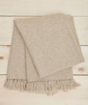 The Large Alpaca Basketweave Throw in beige, featuring super-soft alpaca and fringe edges, is neatly folded on a light wooden surface.