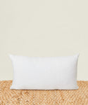 The Linen Lumbar Pillow with a feather down insert sits upright on a textured beige mat against a light cream background.