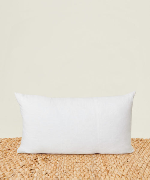 The Linen Lumbar Pillow with a feather down insert sits upright on a textured beige mat against a light cream background.