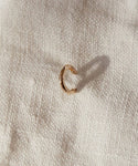 The Huggie, a small rose gold hoop earring, sits on textured off-white fabric, casting a soft shadow—a refined piece of minimalist jewelry.