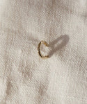 The Huggie, a small 14K gold hoop earring, sits on textured off-white fabric and casts a subtle shadow—ideal for those who love minimalist jewelry.