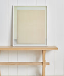 The Untitled 2 Framed Print by Tycjan Knut, featuring soft beige and cream tones, rests on a simple wooden bench against a white paneled wall—an elegant accent inspired by Jenni Kayne Home.