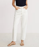 A person stands with hands in the pockets of 90s Crop Jeans, wearing a sleeveless black top and tan sandals, against a plain light background.