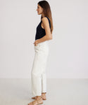 A woman stands in profile against a plain background, wearing a navy sleeveless top, 90s Crop Jean in white high-waisted straight-leg style, and beige sandals, with her hands in her pockets.