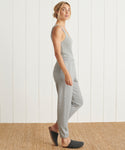 A woman stands sideways on a woven rug in front of a white paneled wall, wearing ultra-soft light gray Saturday Sweatpants and dark gray slippers.