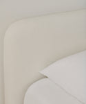Close-up of a bed featuring the Cove Bed Slipcover in soft, light beige upholstery with crisp white Belgian Libeco linen bedding, neatly arranged pillow and sheet, for a minimalistic and modern look.
