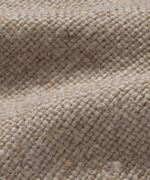 Close-up of the Miramar Sofa Slipcover’s coarse, woven burlap fabric in natural beige, highlighting its textured surface and rough fibers—reminiscent of Belgian linen—with raised ridges and gentle fold shadows.