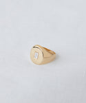 The Gemma Baguette Signet Ring showcases a rectangular baguette-cut diamond set in 14k gold on a light gray fabric background—a classic piece from Jenni Kayne Jewelry.