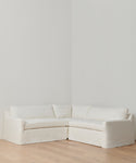 The Harbor Sectional, in Belgian flax linen with plush cushions, sits in a corner on light wood floors and against white walls—a classic sofa choice for any room.