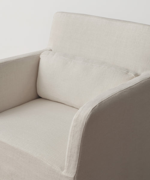 The Sunset Dining Arm Chair Slipcover in sandstone linen adds elegance to a beige upholstered armchair with clean lines, a modern minimalist design, and a matching rectangular cushion, shown against a plain white background.